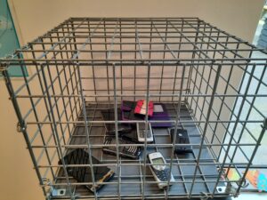 A wire box on a plinth containing a set of disused mobile phones for recycling. Some phones also have covers, including one with a pink smiley face on it.