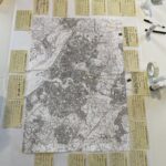An A1 map of Southampton (black and white) is set out on a table and surrounded by arts supplies, mobile phones, and a set of 'archive tags' on which people can write their memories. Each tag has 'Telephonic Youth Archive' printed on it.