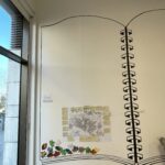 The A1 map and memories stuck onto a wall with a large outline in the form of a wirebound book painted on it. Other small artworks are also included in the book, including some painted leaf shapes. To the left is a large window looking out onto a public open space.