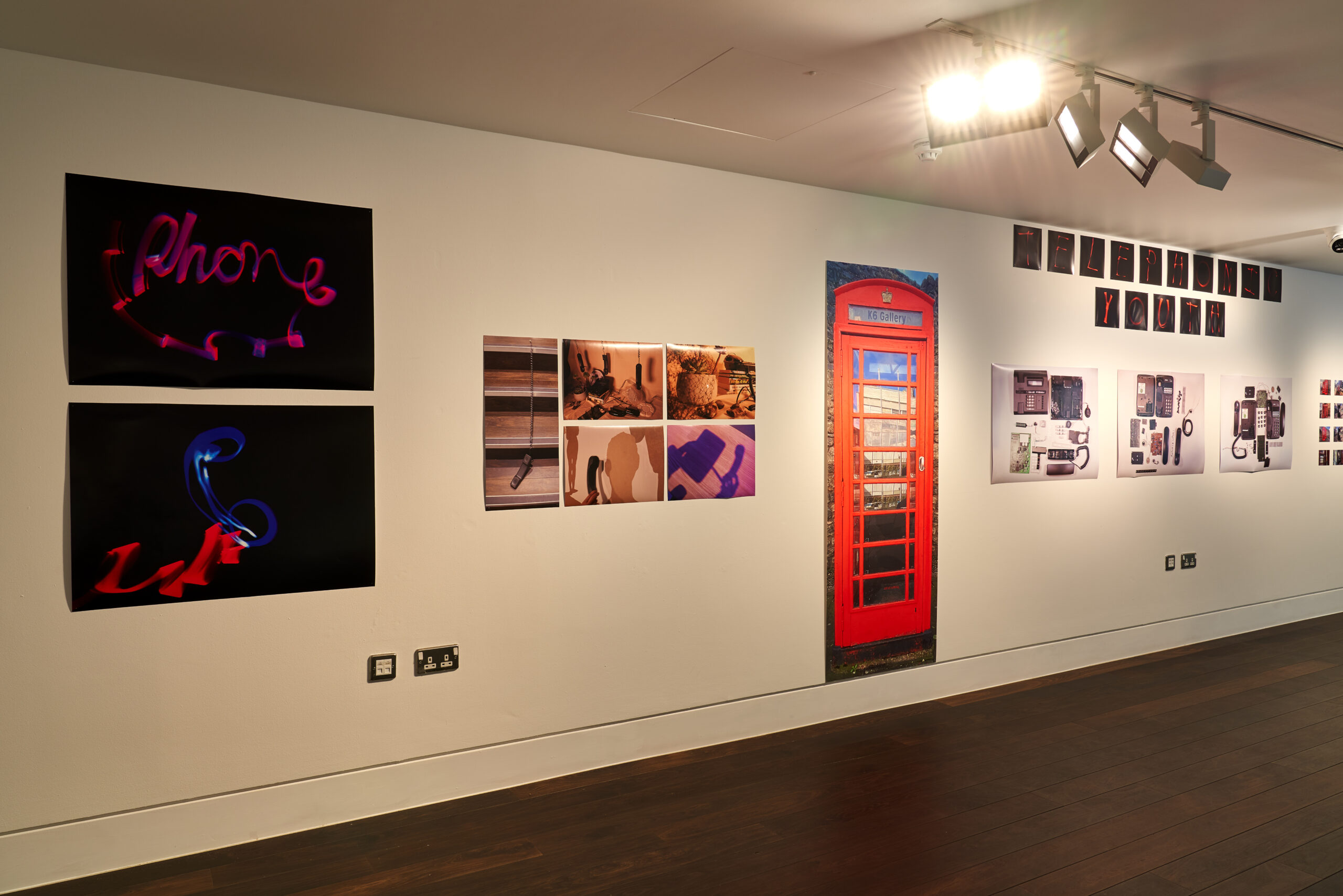 A series of photographs on a white gallery wall. The photos include the word 'phone' created using light, a large portrait image of a red telephone box, and a series of photos of disassembled telephones.